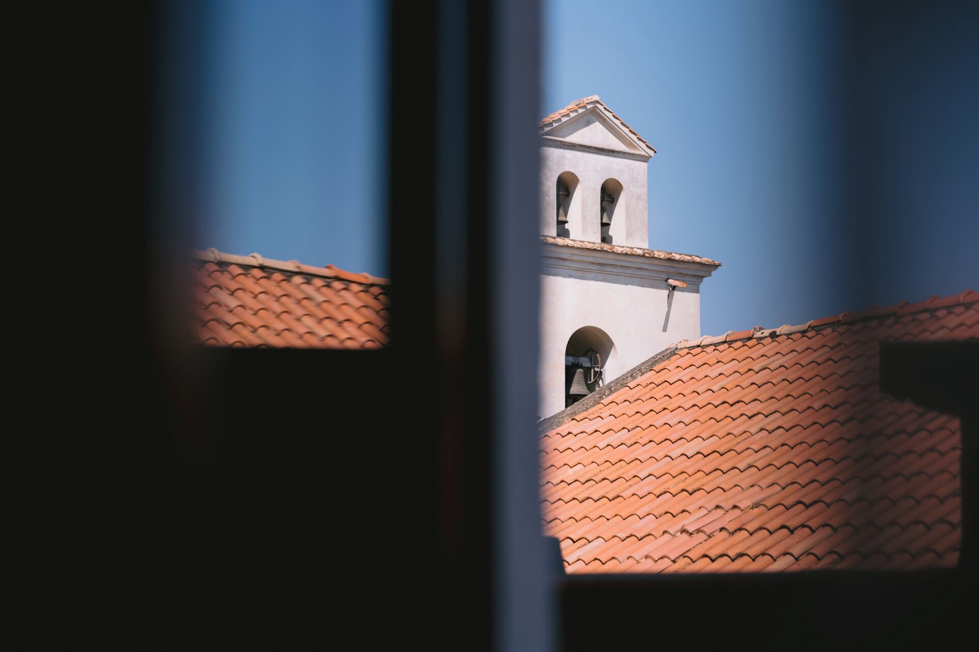 A bell tower with a tiled roof, viewed through a window frame.