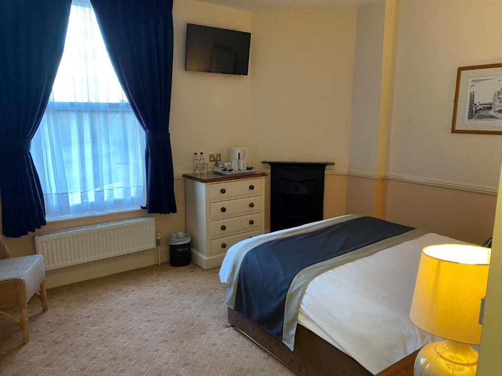 A hotel room with a bed, a dresser, a radiator, a TV, and a lamp.