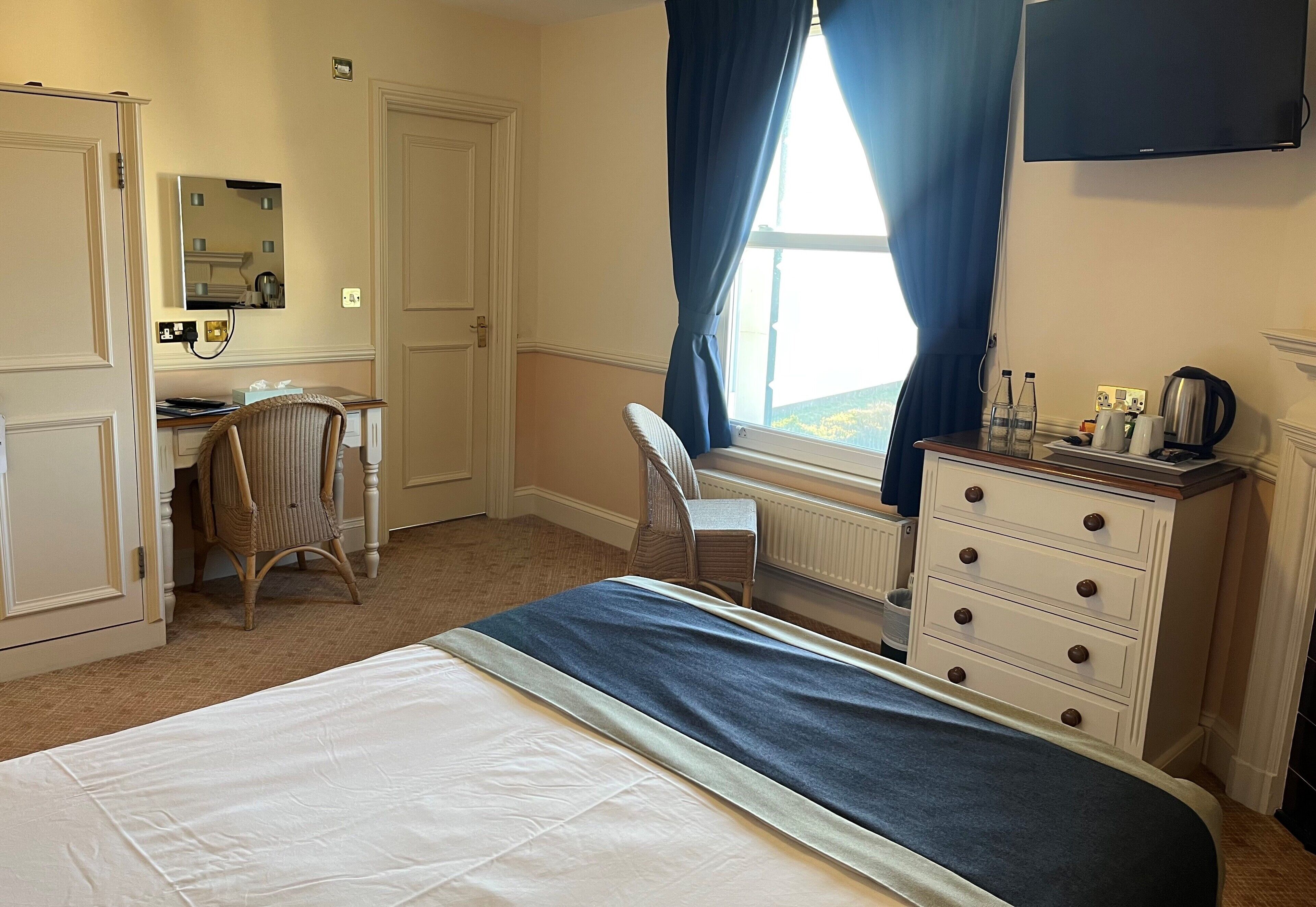 A hotel room with a bed, a desk, a chair, a dresser, and a television.
