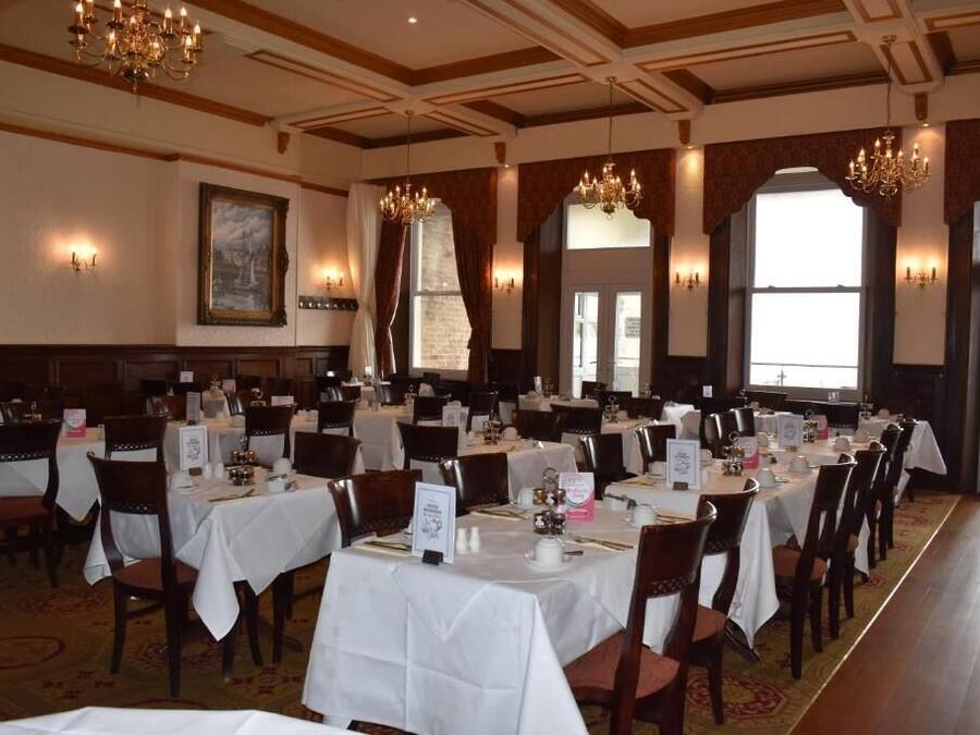 Een feestzaal met gedekte tafels, kroonluchters en grote ramen.
