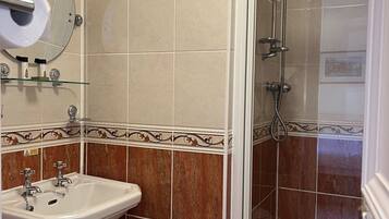 Ein Badezimmer mit Waschbecken, Spiegel, Toilettenpapierhalter und Duschbereich.