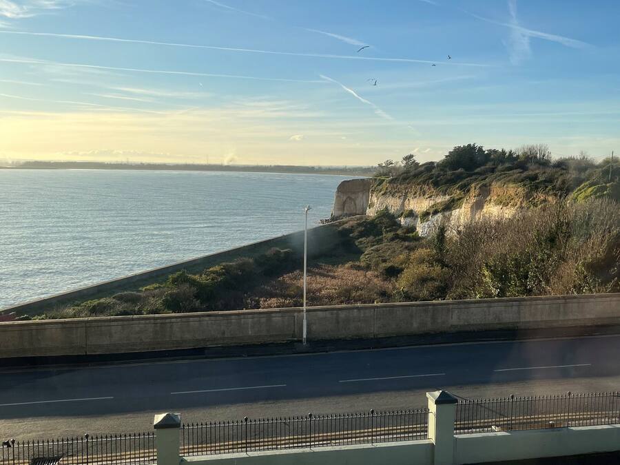 A coastal road with a concrete barrier, a paved road, and a grassy embankment.
