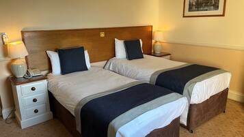 Habitación de hotel con dos camas, cabecero de madera, mesitas de noche con lámparas y un cuadro enmarcado en la pared.
