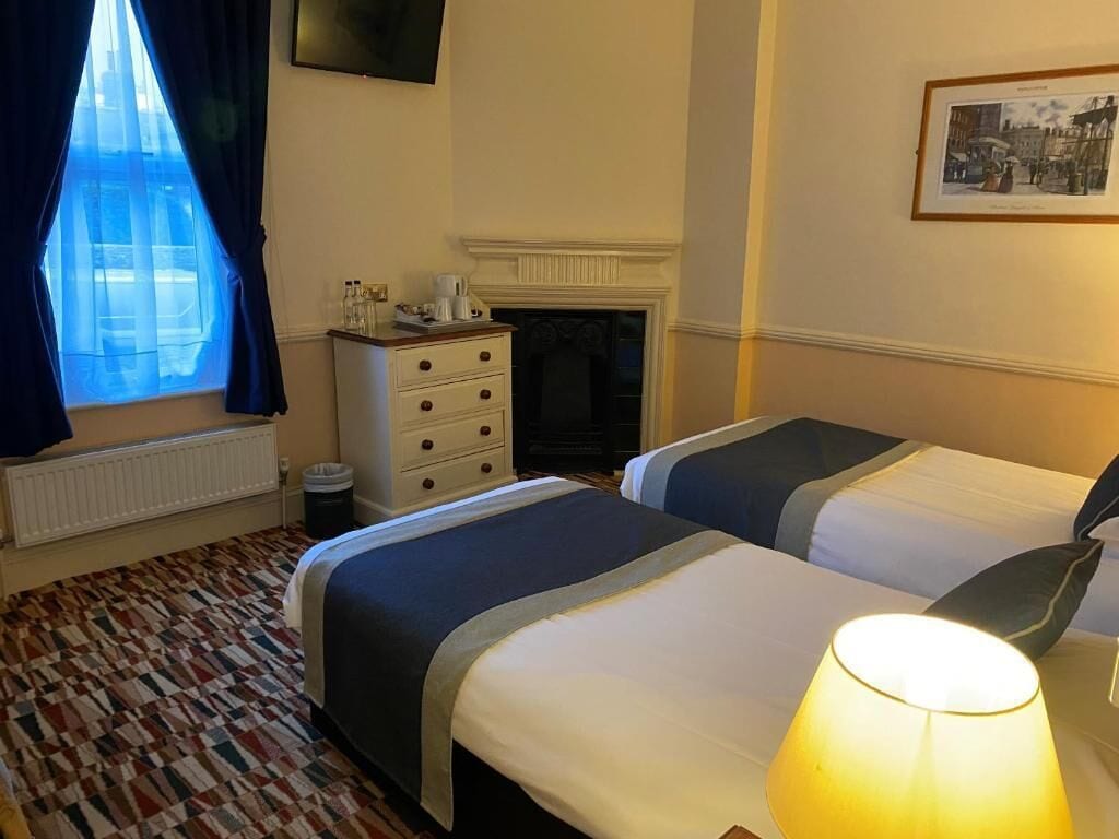 A hotel room with two beds, a dresser, a fireplace, and a window with curtains.