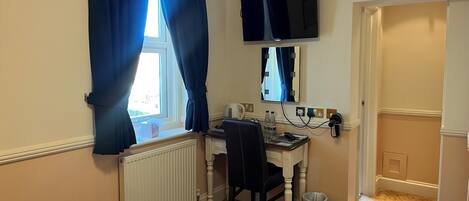 A hotel room with a bed, a desk with a chair, a television mounted on the wall, and a window with curtains.