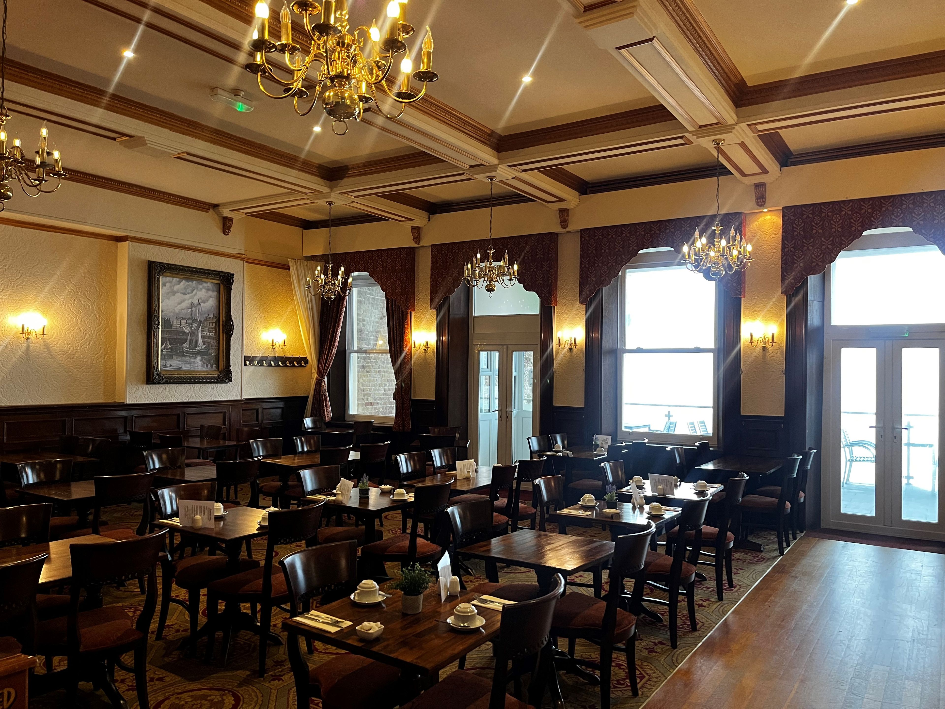 A restaurant with multiple tables and chairs, chandeliers, and large windows.