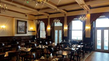 A restaurant with multiple tables and chairs, chandeliers, and large windows.
