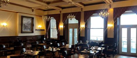 A restaurant with multiple tables and chairs, chandeliers, and large windows.