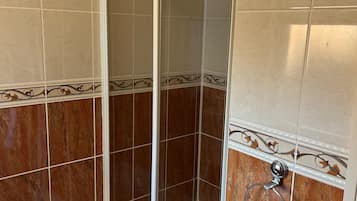 Ducha con puerta de vidrio, una toalla blanca colgada de un aro metálico y suelo de baldosas.