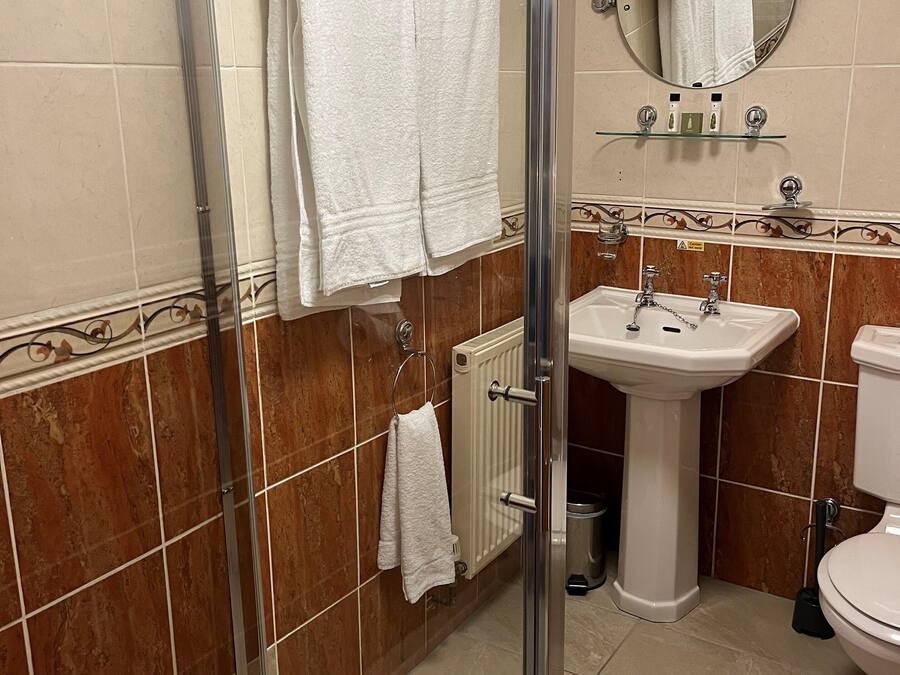 Un baño con cabina de ducha de vidrio, lavamanos pedestal, inodoro y espejo sobre el lavamanos.
