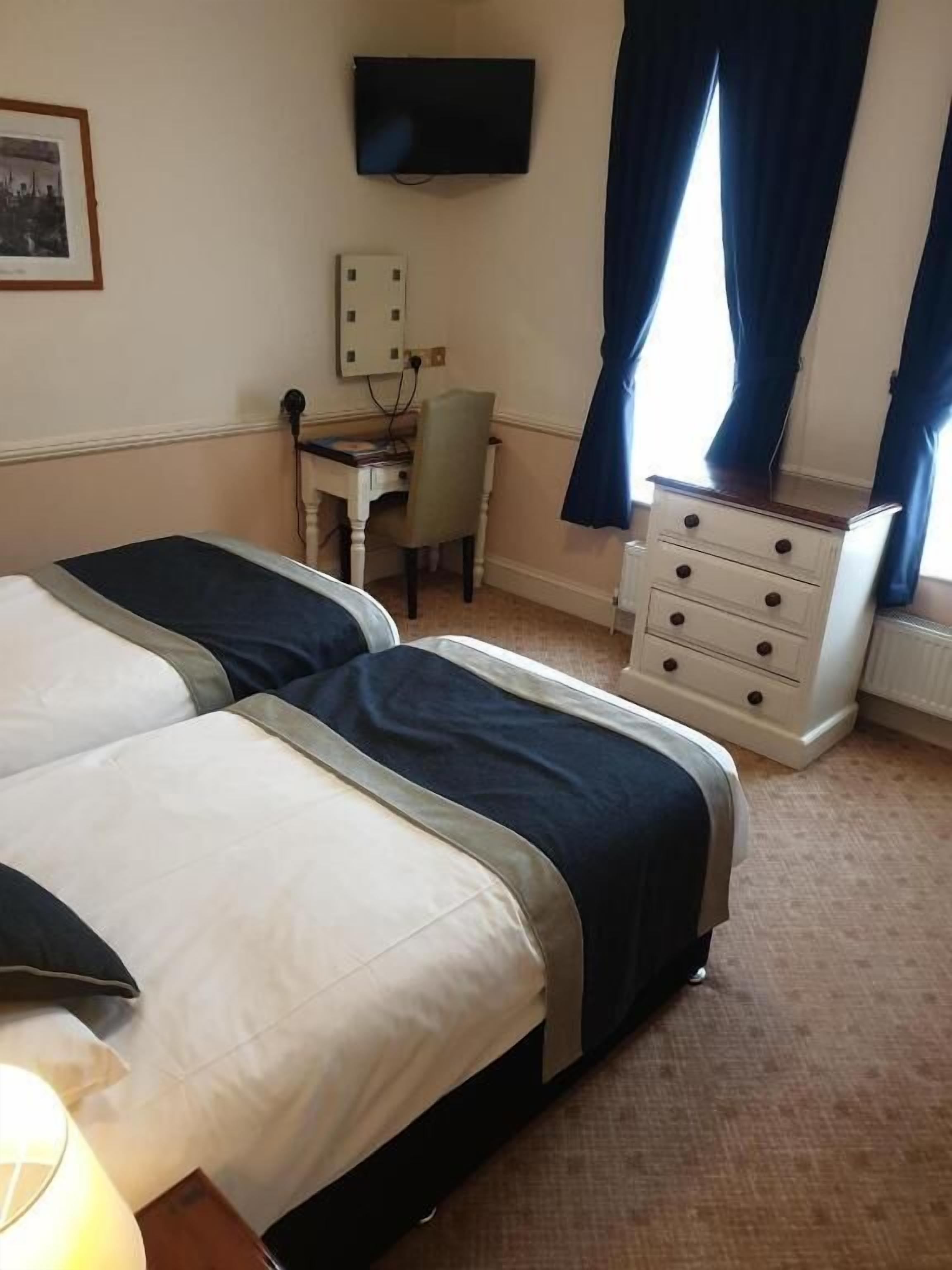 Een hotelkamer met twee bedden, een bureau met stoel, een dressoir, een televisie en een raam met gordijnen.