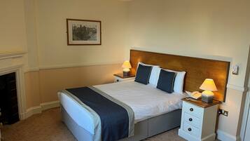 A neatly arranged bedroom with a large bed, bedside tables with lamps, a nightstand, and a framed picture on the wall.