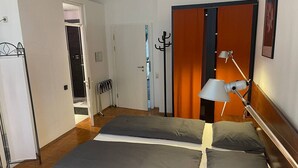 A hotel room with two beds, a coat rack, a lamp, and a door leading to another room. - Studio for 2 in Konstanz (Konstanz)