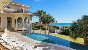 A pool area with lounge chairs, a palm tree, and a view of the ocean.