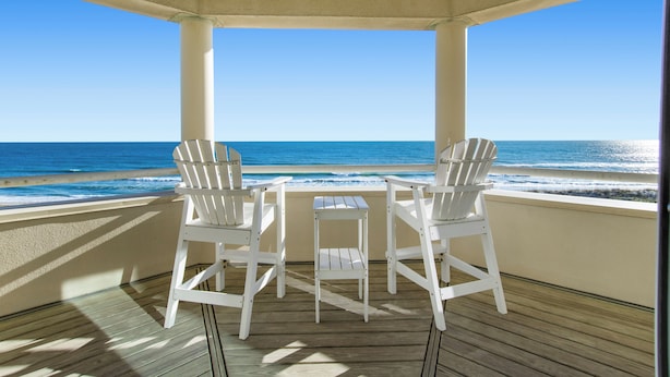 A covered outdoor seating area with two white chairs and a small table, overlooking the ocean.