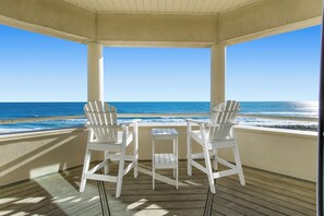 A covered outdoor seating area with two white chairs and a small table, overlooking the ocean. - Expansive 10 BR Oceanfront Estate with Infinity Pool, Theater & Grand Spaces (Indian Beach)