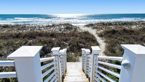 A wooden staircase leading to a beach with white railings and a clear view of the ocean.