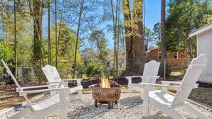 A patio area with Adirondack chairs and a fire pit surrounded by white gravel. - Chic 3BR Retreat•Firepit•Minutes to NC State (Raleigh)