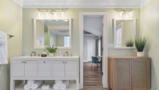 A bathroom with a white vanity, a mirror, and a wooden cabinet. - Chic 3BR Retreat•Firepit•Minutes to NC State (Raleigh)