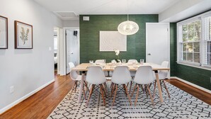 A dining area with a wooden table, white chairs, and a patterned rug. - Chic 3BR Retreat•Firepit•Minutes to NC State (Raleigh)