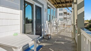 Eine überdachte Terrasse mit Tisch und Stühlen, Holzgeländern und Blick auf ein mehrgeschossiges Gebäude im Hintergrund.