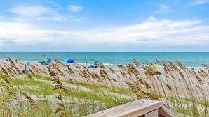 Ein Strand mit Holzterrasse, Sonnenschirmen und hohem Gras.
