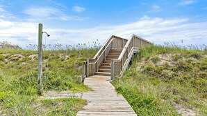 Eine Holztreppe führt zu einem Gebäude an einem sandigen Strand, der von einem klaren Himmel überdacht wird.