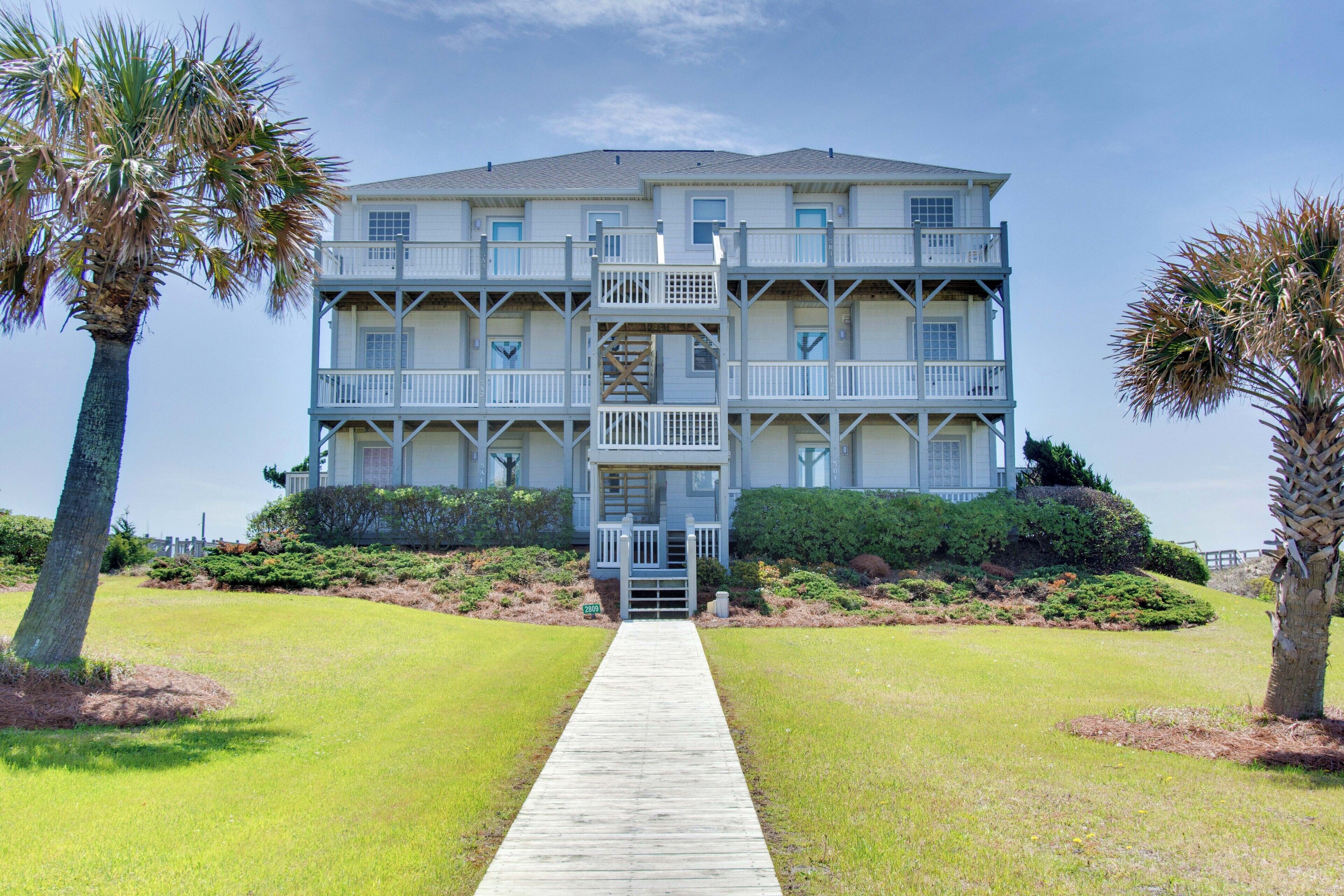 A multi-story building with a central staircase, surrounded by well-maintained lawns and palm trees.