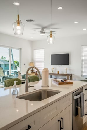 Una cocina moderna con una isla grande, pileta de acero inoxidable y luces colgantes.