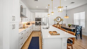 A modern kitchen with white cabinetry, a central island, pendant lighting, and a dining area with wooden chairs and a table.