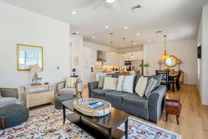 A modern living room with a grey sofa, a coffee table, and a dining area with a chandelier.