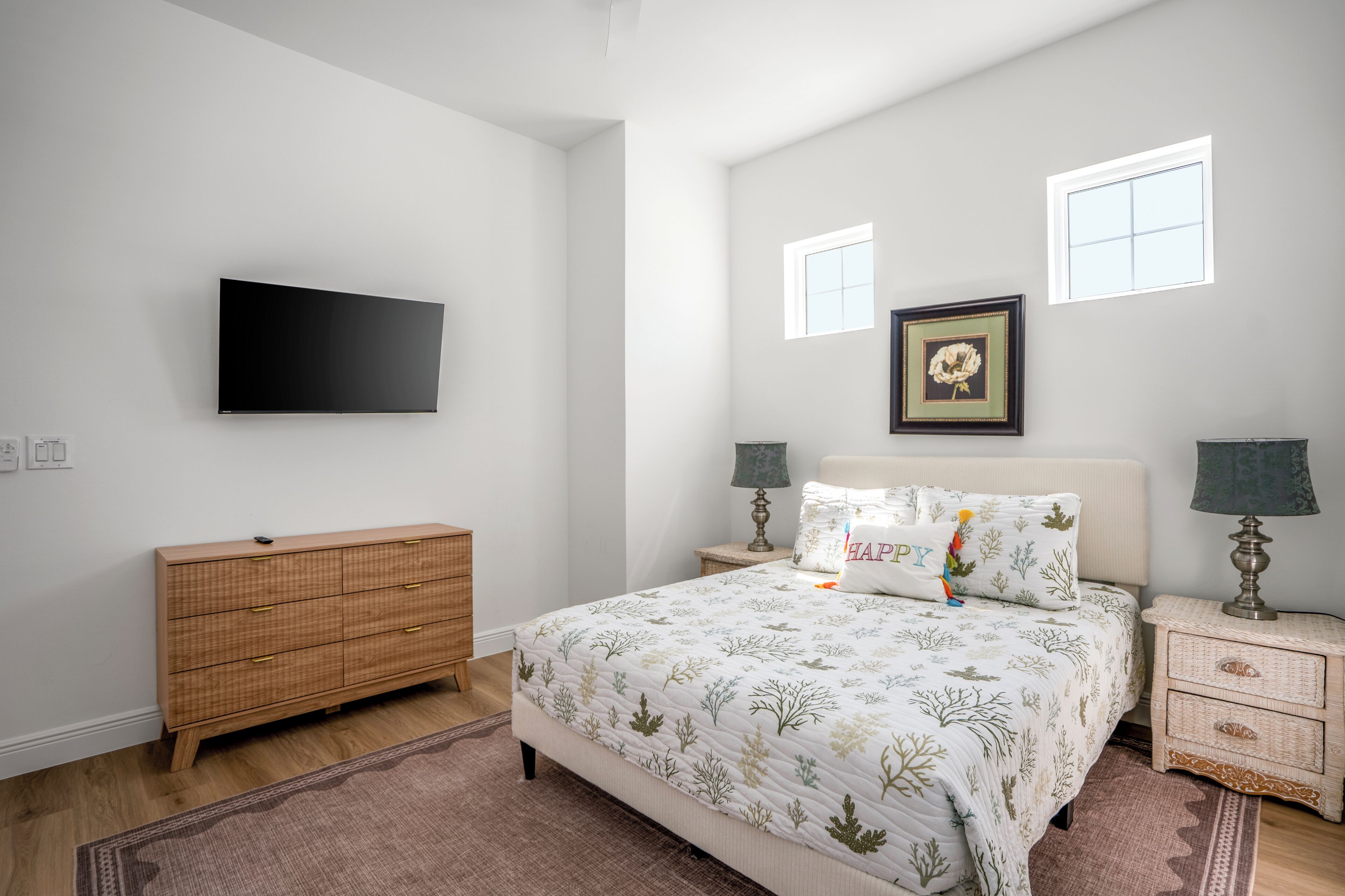 Une chambre à coucher comprenant un lit, une commode, un téléviseur, deux tables de chevet avec des lampes et un tableau encadré au mur.