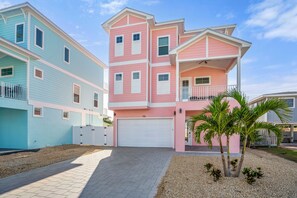 A multi-story residential building with a garage, a balcony, and a small palm tree in the front yard.