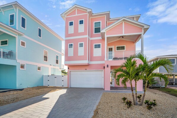 A multi-story residential building with a garage, a balcony, and a small palm tree in the front yard.