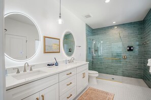A modern bathroom with a large vanity, two round mirrors, a shower with a glass enclosure, and a toilet.