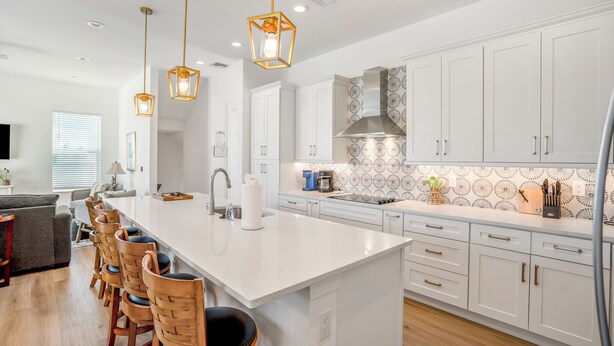 A modern kitchen with white cabinets, a central island with bar stools, pendant lighting, and a backsplash with a circular pattern.