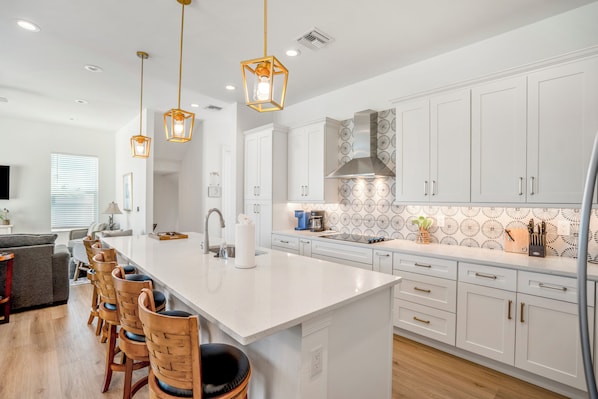 A modern kitchen with white cabinets, a central island with bar stools, pendant lighting, and a backsplash with a circular pattern.