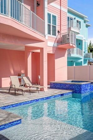 A swimming pool with a tiled edge, lounge chairs, and a building with balconies.