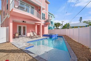 A two-story house with a swimming pool, a balcony, and a patio with chairs.