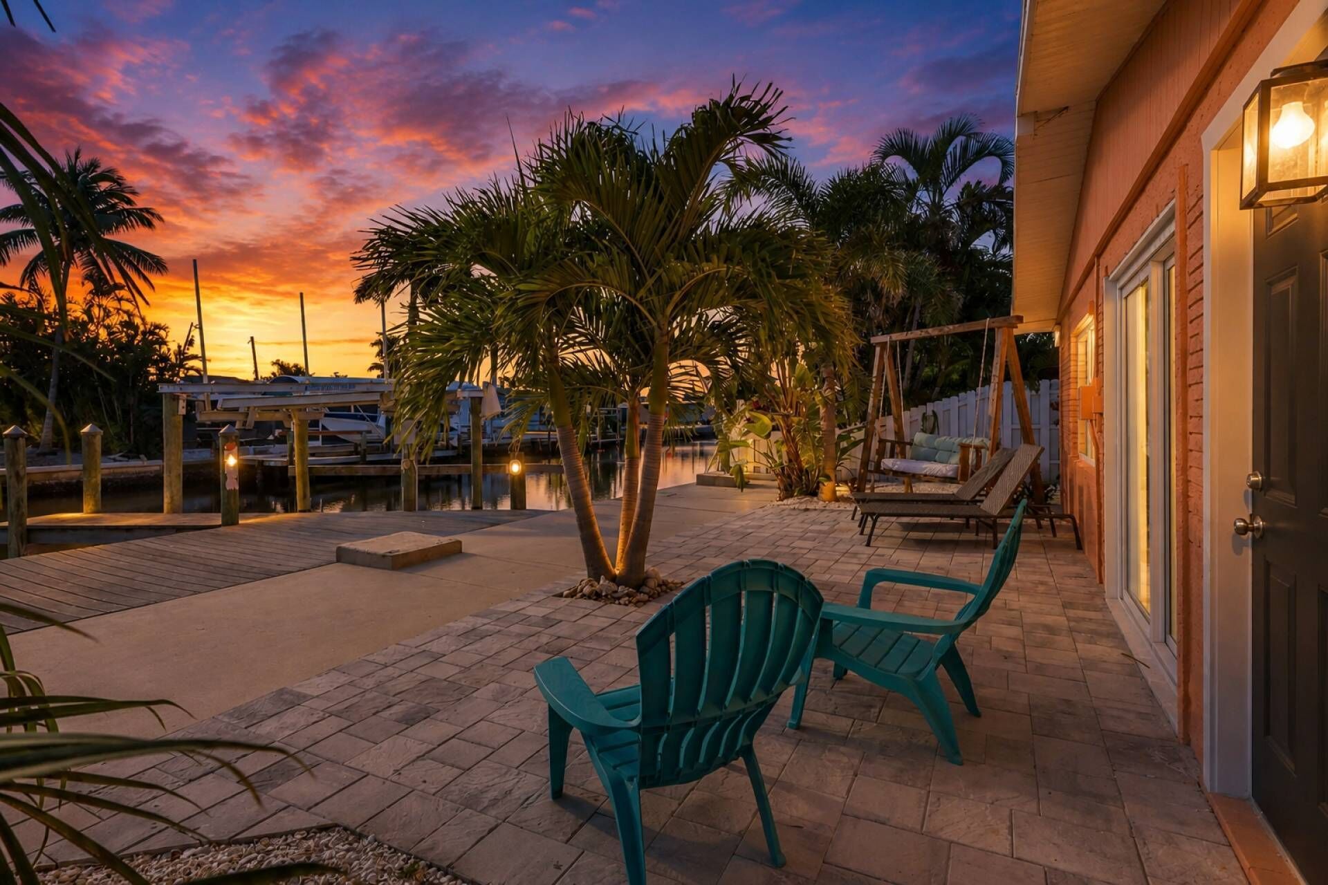 A patio with chairs, a swing, and a view of the marina at sunset.