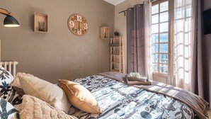 Ein Schlafzimmer mit einem Bett, einer Holzuhr, einem Regal und einem Fenster mit Vorhängen.