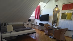 Quarto estilo loft com cama, escrivaninha, cadeira e televisão.