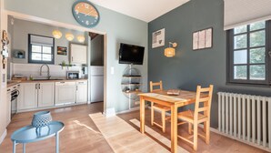 A modern kitchen with white cabinets, a wooden dining table, and a TV mounted on the wall. - Gîte le Tech Nordic Bath & Sauna in the Heart of the Mountains (Arrens-Marsous)
