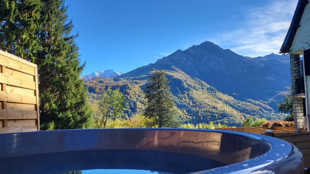 A hot tub with a mountain view, wooden deck, and a stone building. - Gîte le Tech Nordic Bath & Sauna in the Heart of the Mountains (Arrens-Marsous)