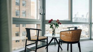 Una habitación moderna con un ventanal grande, dos sillas, una mesita redonda y un florero con flores.