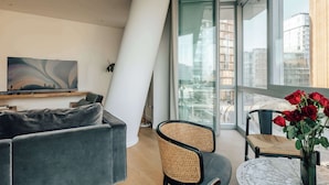 Una sala de estar moderna con un sofá, una butaca, una mesa con un jarrón de rosas rojas y un ventanal con vistas a la ciudad.