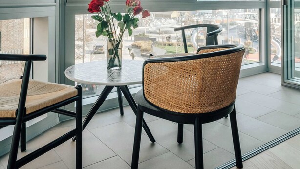 Un comedor moderno con una mesa redonda, dos sillas de mimbre y un jarrón con flores rojas.