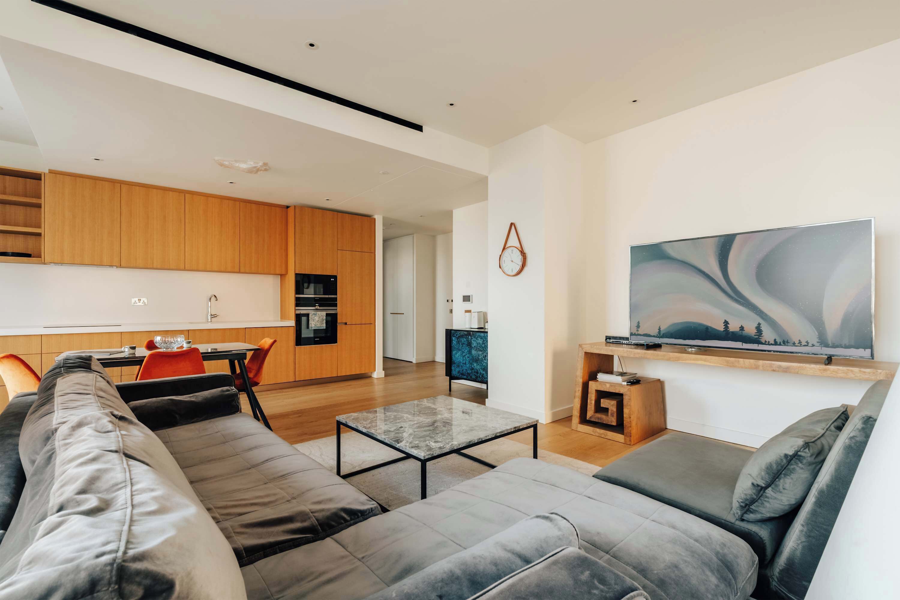Ein modernes Wohnzimmer mit grauem Sofa, einem Couchtisch und einem an der Wand befestigten Fernseher.