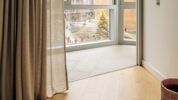Ein modernes Zimmer mit einer großen Schiebeglas-Tür, die auf einen Balkon im Freien führt, Holzböden und einem Blumentopf.