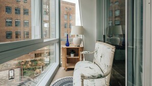 Ein Zimmer mit einem großen Fenster, einem weißen Sofa, einer Lampe und einem kleinen Holztisch mit einer blauen Vase.